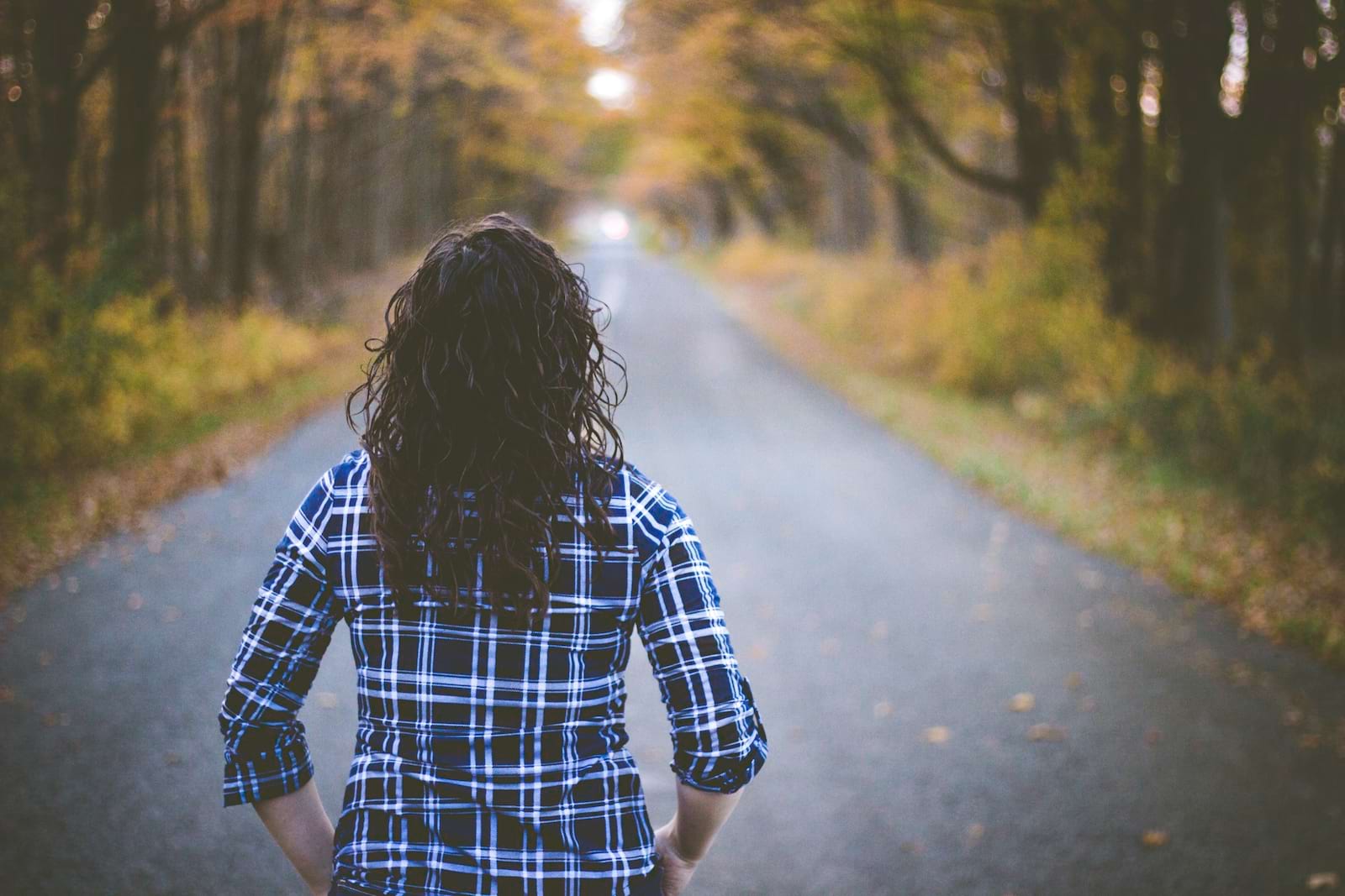 Woman walking down a countryside tee lined road